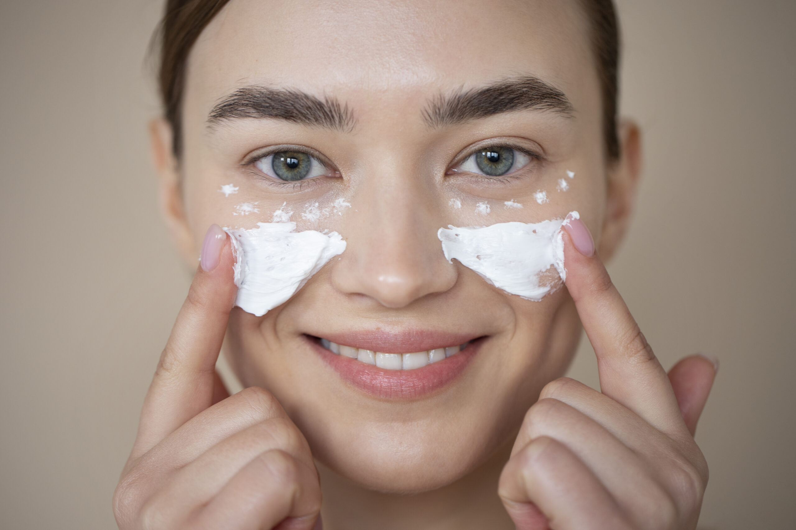 Close-up of woman applying under-eye cream and moisturizer to her face with a smile